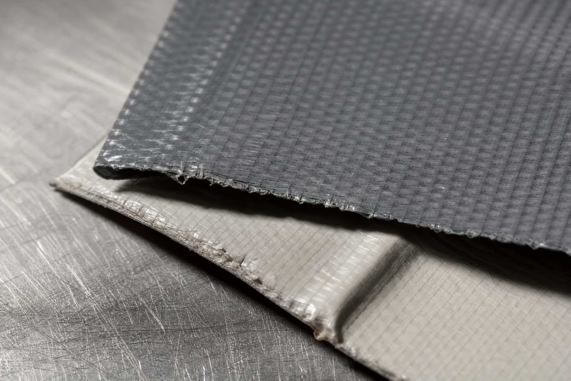 PVC tarpaulin material samples overlapping on a steel workbench