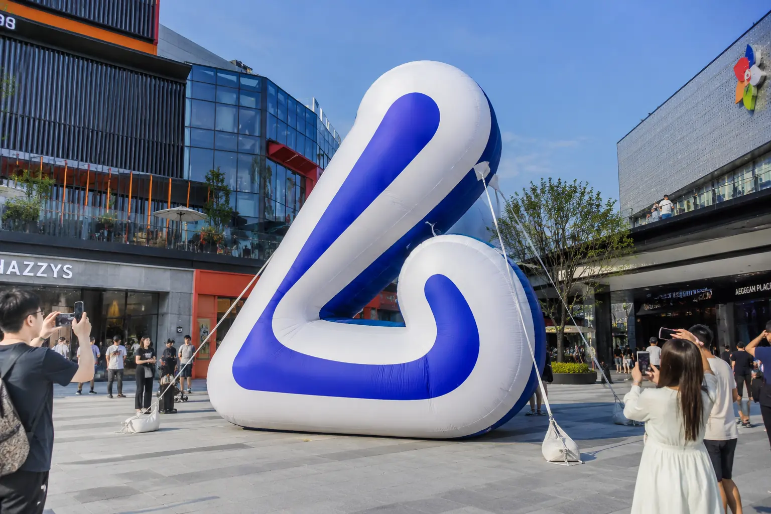 Large custom inflatable logo display installed in an outdoor shopping plaza for brand advertising